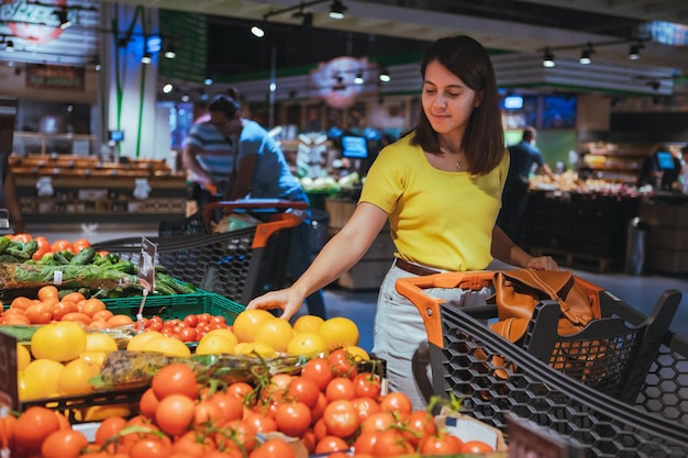 Donna che sceglie i pomodori gialli dallo scaffale del negozio a fare la spesa