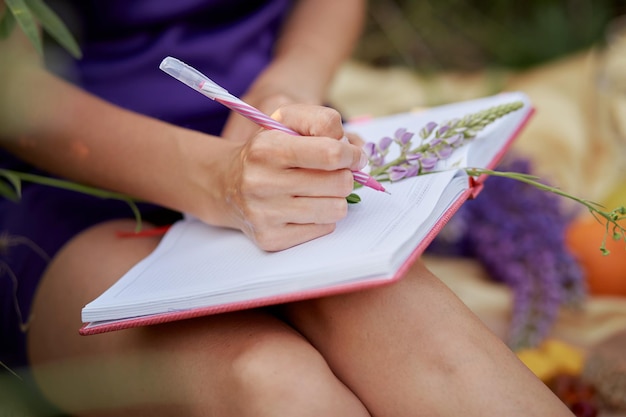 Donna che scrive in quaderno con bouquet di fiori di campo lupini Vicinanza alla scoperta di sé stessi della natura