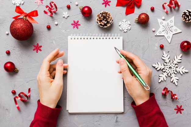 Donna che scrive la lista delle cose da fare di Natale sul taccuino su sfondo colorato con decorazioni natalizie