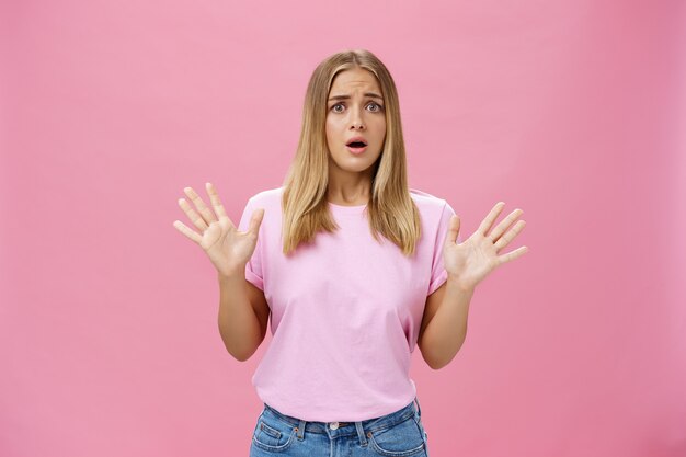 Donna che sembra nervosa spiegando con gesti di panico contro il muro rosa.