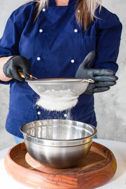 Donna che setaccia la farina attraverso un vecchio setaccio sulla tavola della cucina