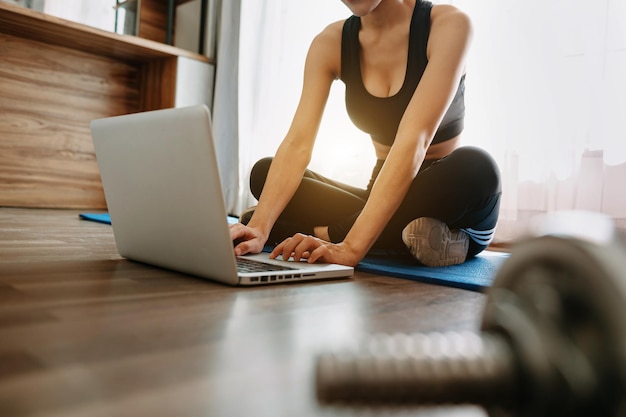 Donna che si esercita a casa e guarda video di allenamento con manubri e guarda il laptop. Bella donna in abbigliamento sportivo