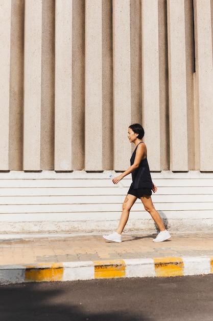 Donna che si esercita camminando per strada con la mano in mano una bottiglia d'acqua