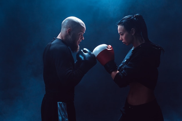 Donna che si esercita con il trainer alla lezione di boxe e autodifesa, studio, fumo nello spazio