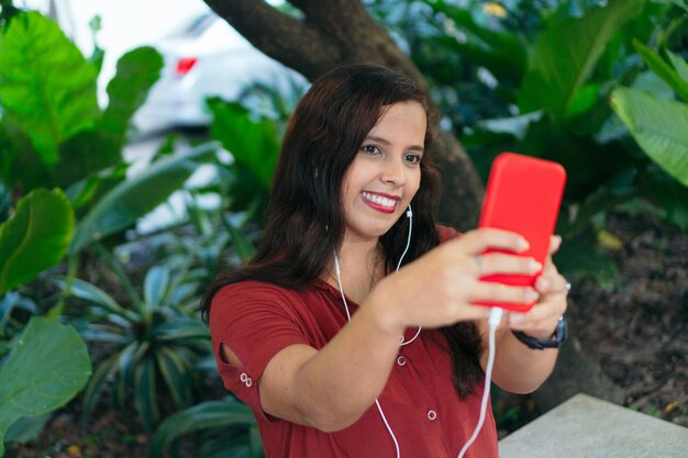 Donna che si fa un selfie con il suo smartphone in una videochiamata del parco e un concetto di vlogger