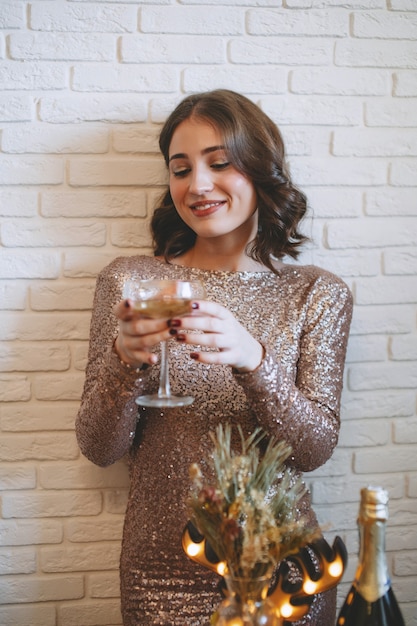 Donna che si gode la festa di capodanno a casa Ragazza elegante alla moda che beve champagne sotto i coriandoli a casa