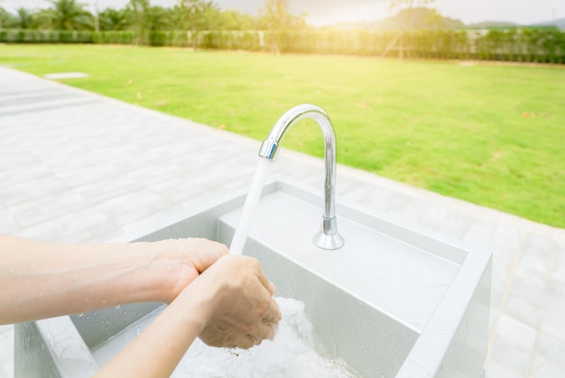 Donna che si lava le mani con l'acqua del rubinetto sotto il rubinetto al lavandino bianco Lavarsi le mani con l'acqua del rubinetto al lavandino