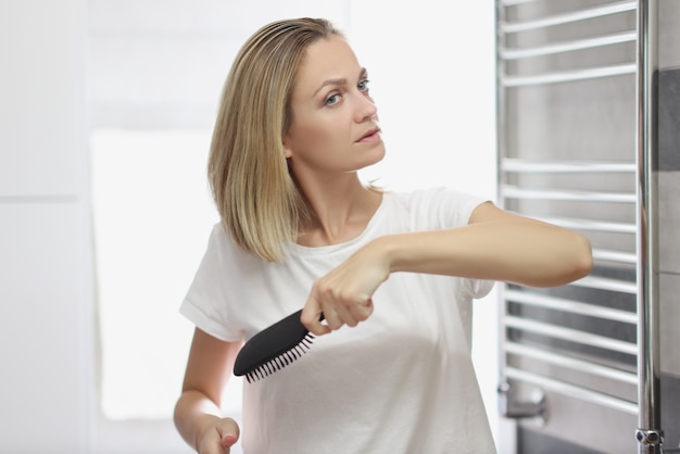 Donna che si pettina i capelli con il pettine in bagno davanti allo specchio