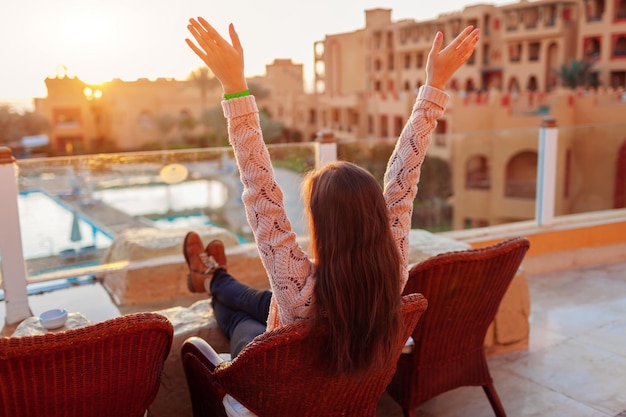 Donna che si rilassa al balcone dell'hotel godendosi l'alba con piscina e vista mare Ragazza felice che alza le braccia