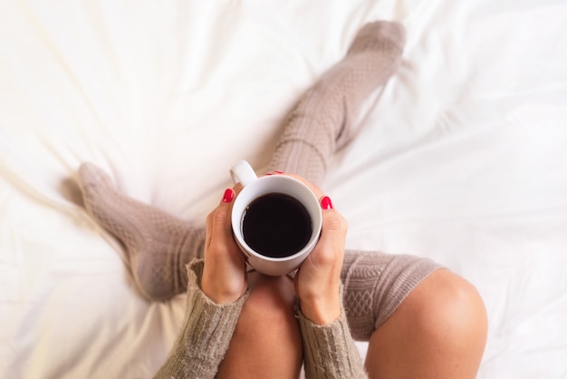 Donna che si siede a letto bevendo una tazza di caffè