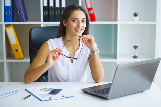 Donna che si siede allo scrittorio, lavorando al computer portatile in ufficio moderno