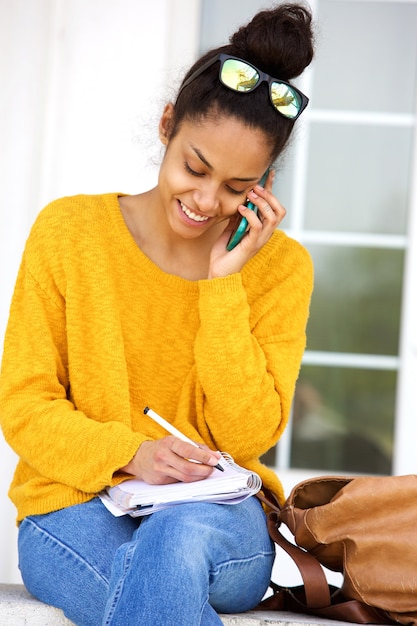 Donna che si siede fuori del libro di scrittura e che parla sul telefono cellulare