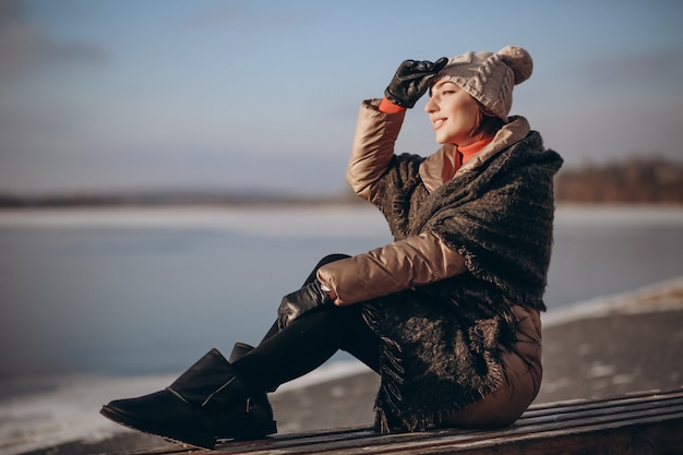 Donna che si siede su una panchina sul lago in inverno