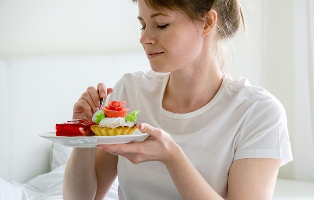 Donna che si siede sul letto e che mangia le torte