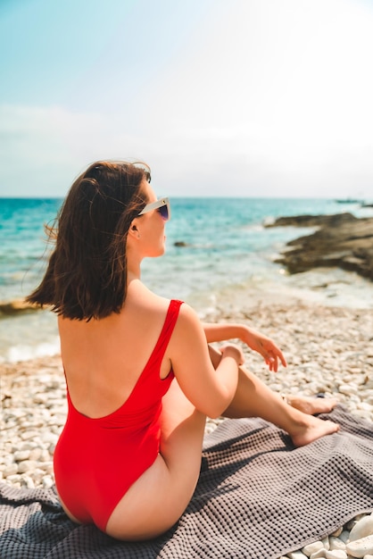 Donna che si siede sulla coperta al concetto di vacanza estiva della spiaggia del mare