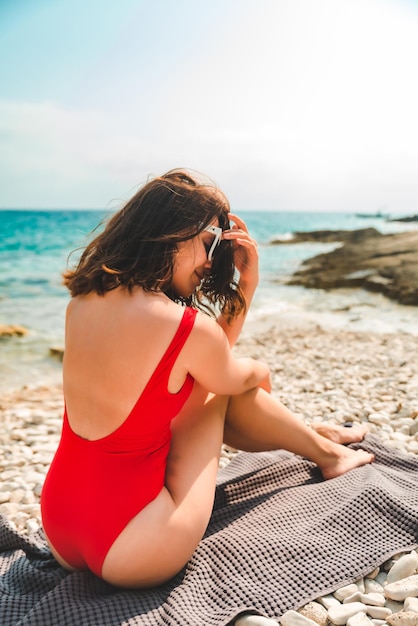 Donna che si siede sulla coperta al concetto di vacanza estiva della spiaggia del mare