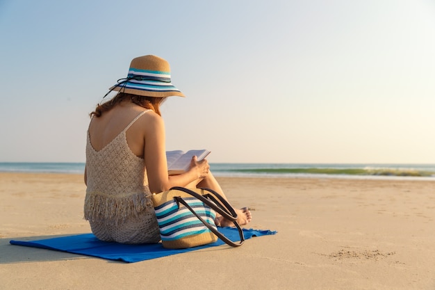 Donna che si siede sulla spiaggia e sul libro di lettura