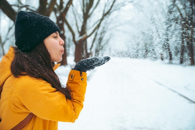 Donna che soffia neve dalle sue mani. parco innevato sullo sfondo. concetto di stagione invernale