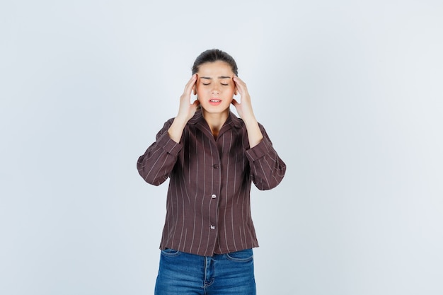 donna che soffre di emicrania in camicia, jeans e dall'aspetto angosciato, vista frontale.