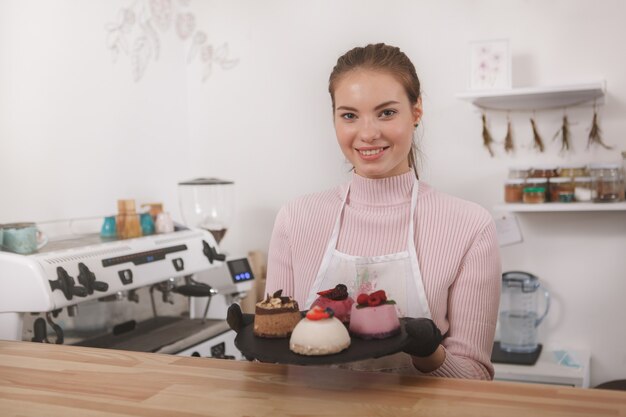 Donna che sorride alla telecamera, che serve deliziosi dessert nella sua caffetteria