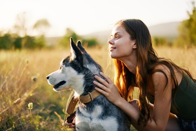 Donna che sorride e abbraccia il suo cane seduto in un campo con un cane bassotto sorridente mentre trascorre del tempo all'aperto con un cane amico in autunno al tramonto durante il viaggio