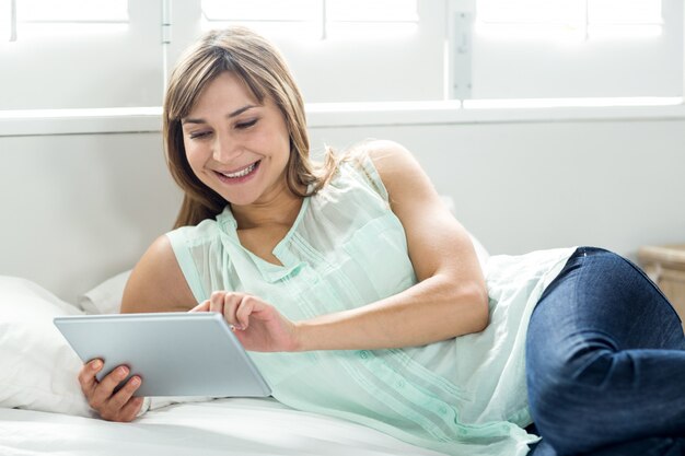 Donna che sorride mentre per mezzo della compressa digitale sul letto