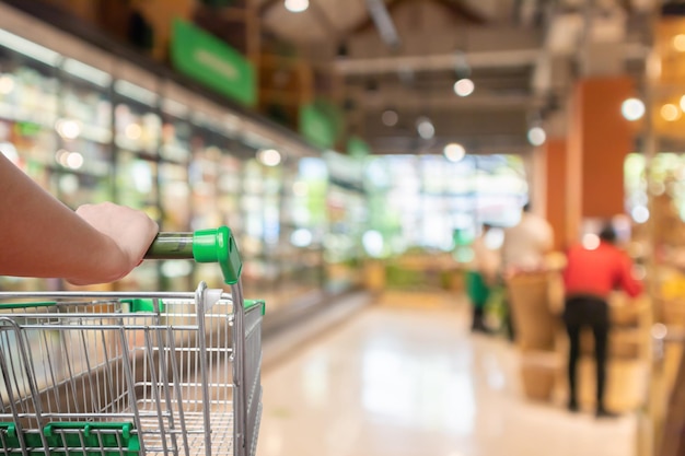 Donna che spinge il carrello con sfocatura dello sfondo del corridoio del supermercato