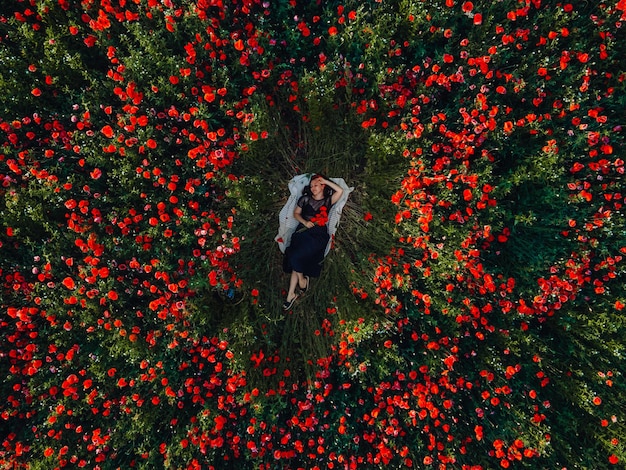 Donna che stabilisce nel mezzo del campo di fiori di papaveri in fiore direttamente sopra