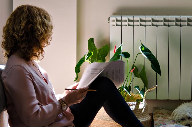 Donna che studia a casa, sdraiata sul divano di casa accanto alla finestra