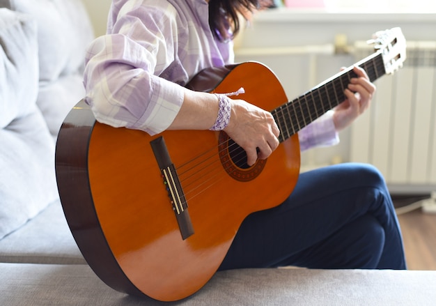 Donna che suona la chitarra seduta su un divano a casa