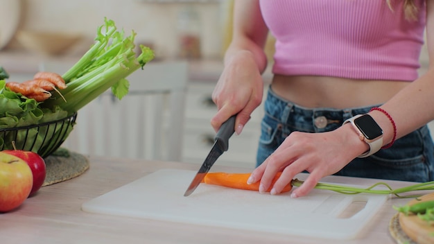 Donna che taglia la carota sulla tavola in cucina Mangiare sano e concetto di cucina