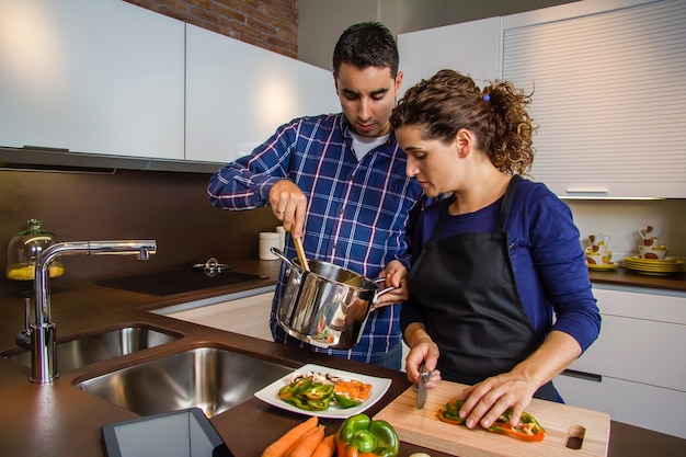 Donna che taglia le verdure mentre suo marito le mostra la pentola con il cibo