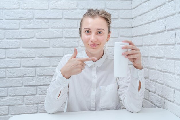 Donna che ti offre un prodotto cosmetico con sfondo bianco muro di mattoni