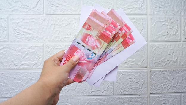 Donna che tiene banconote indonesiane con busta bianca Concetto di valuta rupia contro il muro bianco