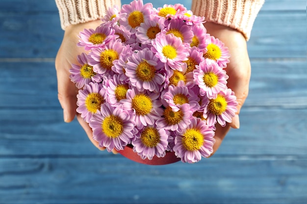 Donna che tiene bei fiori in confezione regalo su fondo di legno