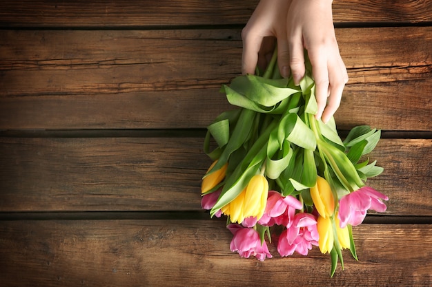 Donna che tiene bellissimi tulipani su una superficie di legno