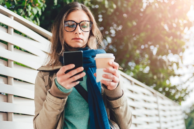 Donna che tiene caffè asportabile e che per mezzo dello Smart Phone