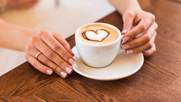 donna che tiene calda tazza di caffè, a forma di cuore