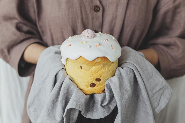 Donna che tiene elegante torta di pasqua appena sfornata con glassa di zucchero e spruzza in tovagliolo di lino