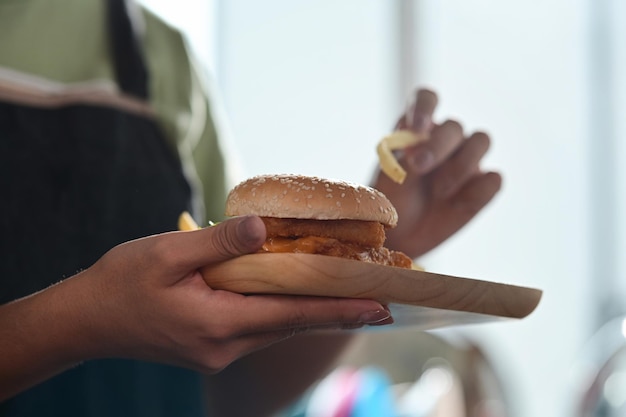 Donna che tiene hamburger di pesce croccante e mangia patate fritte