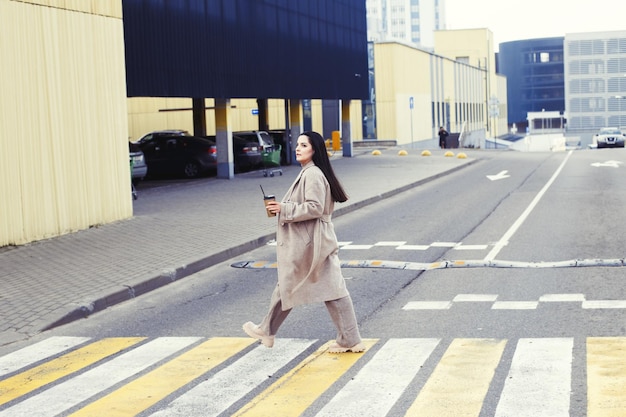 Donna che tiene il caffè e attraversa la strada all'attraversamento pedonale sullo sfondo della città urbana