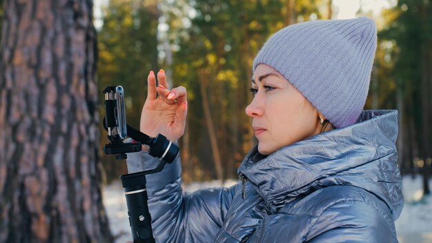 Donna che tiene il dispositivo di stabilizzazione del giunto cardanico a 3 assi con pellicola portatile in inverno per smartphone. Girl Blogger fai selfie, trasmetti video blog, vlogging. Operatore videografo scatta foto video.