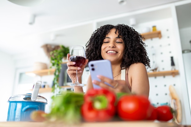 Donna che tiene il telefono cellulare e un bicchiere di vino in cucina a casa