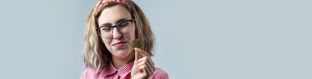 Donna che tiene in mano una criptovaluta bitcoin fisica su sfondo grigio