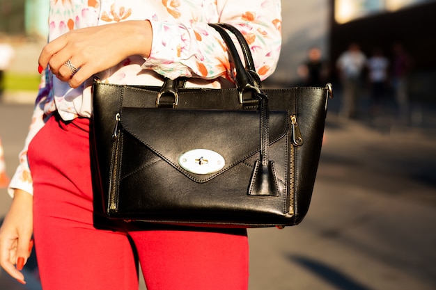 Donna che tiene la borsa di cuoio alla moda che cammina alla città. Primo piano