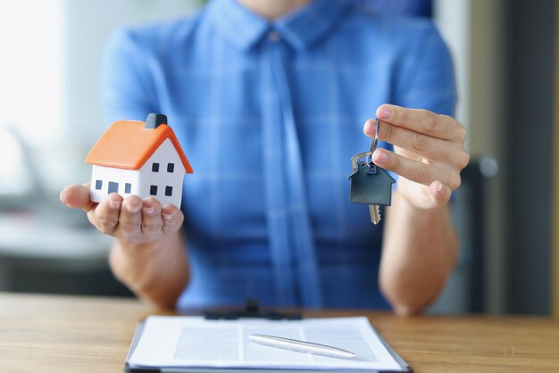 Donna che tiene la casa giocattolo e le chiavi sopra i documenti vendita del primo piano del concetto di immobile residenziale