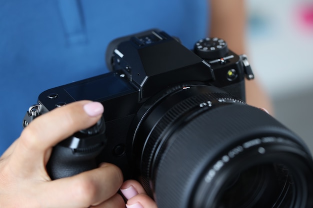 Donna che tiene la macchina fotografica nera professionale nelle mani e raddrizza il primo piano dell'obiettivo