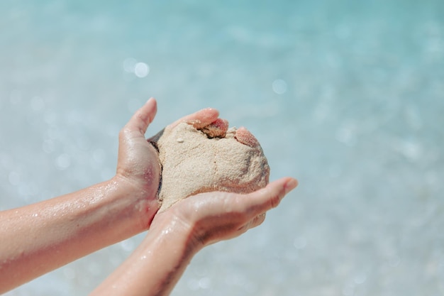 Donna che tiene la sabbia che fa la spiaggia del mare a forma di cuore sullo sfondo