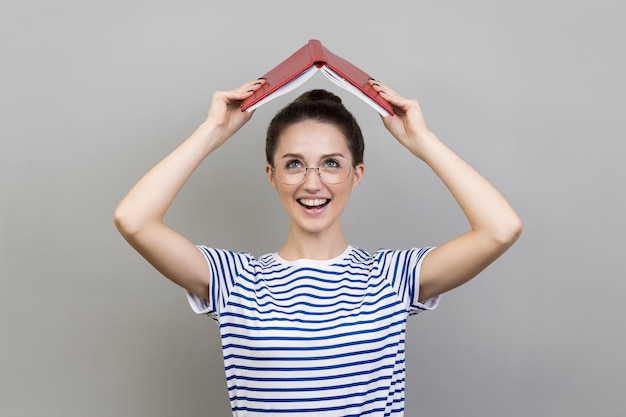 Donna che tiene libro aperto sulla testa che guarda l'obbiettivo con un sorriso che esprime emozioni positive