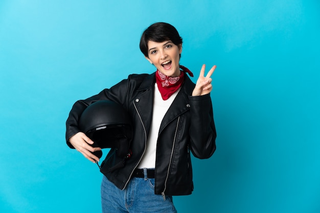 Donna che tiene un casco del motociclo isolato sorridente e mostrando il segno di vittoria